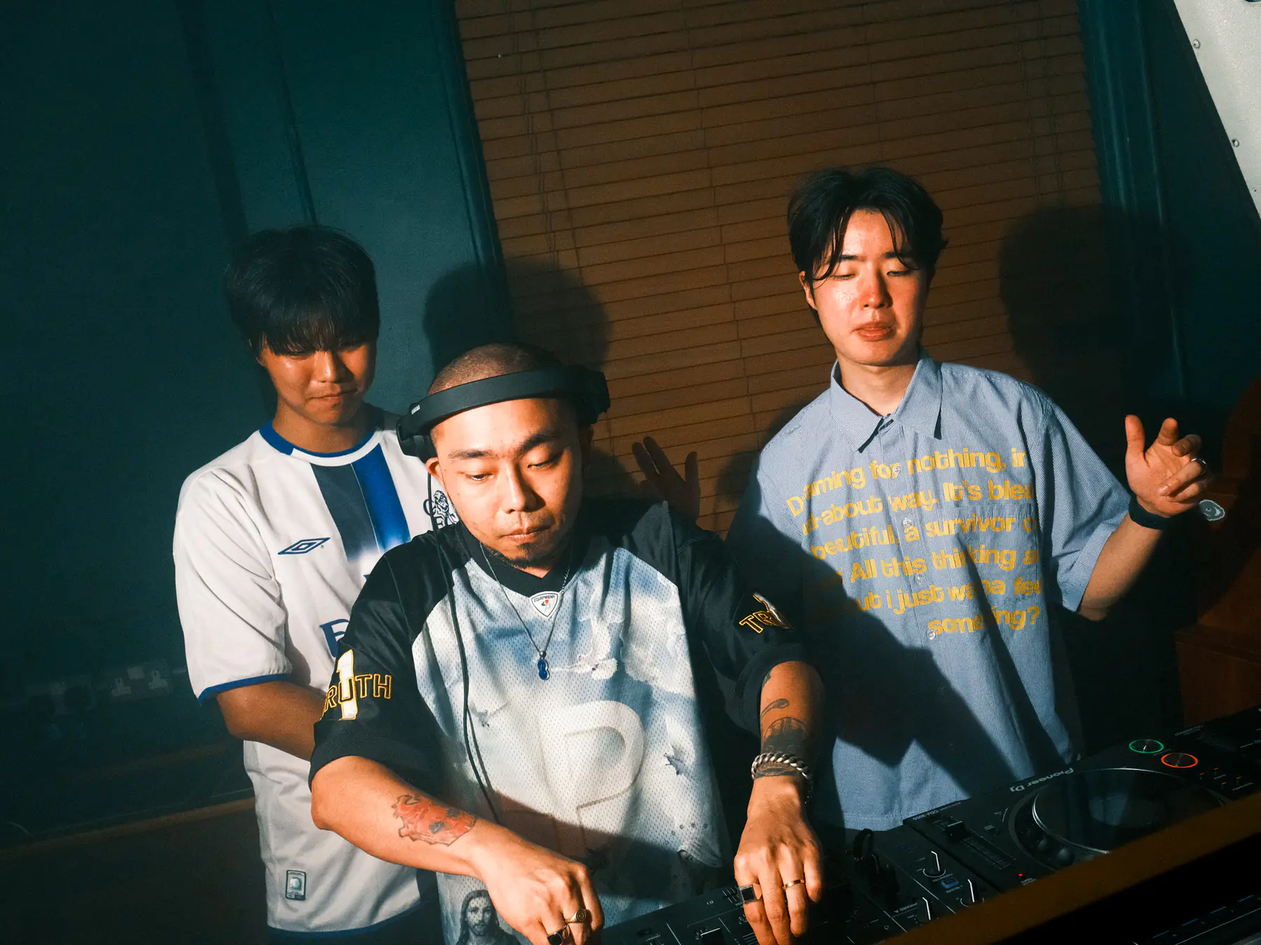 청록색 벽 앞에서 함께 음악을 트는 세 DJ